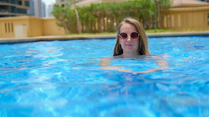 Woman in sunglasses swimming in pool in bikini and enjoing it