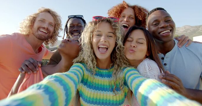 Portrait of happy diverse friends embracing taking group selfie at sunny pool party, slow motion