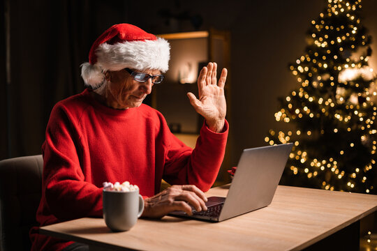 Online Communication And Staying In Touch With Relatives. Grandfather In Santa Hat Sitting At Home During Christmas, Video Calling Family And Waving Hand To Grandkids