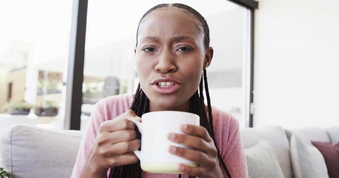 Portrait of happy african american woman with coffee making video call and laughing, in slow motion