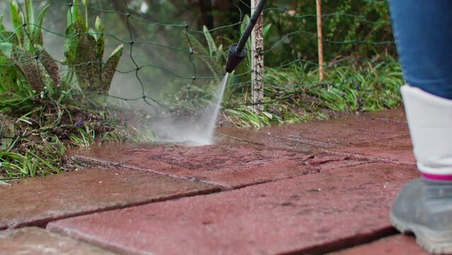 Low angle slow motion shot of cleaning flagstone with a water jet. Boots of worker visible in the foreground. Static slow motion shot, water stream clearly visible.