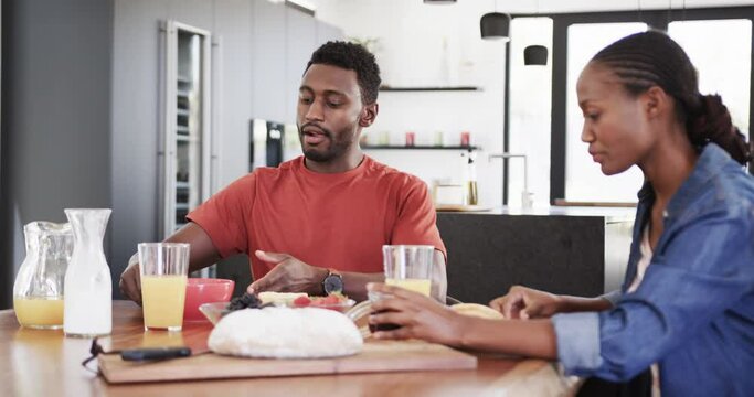 Happy african american couple serving and eating breakfast at table in kitchen, slow motion