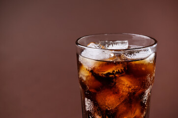 A glass of cola drink with ice cubes. Fresh cold sweet cola drink with ice on brown background with copy space.