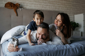 Family is lying on the bed communicating via video on the phone