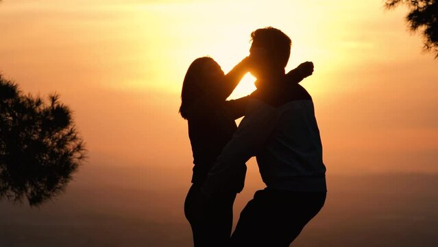 Silhouette of kissing couple against sunset at mountain top