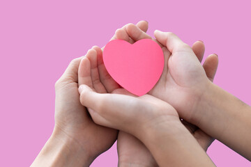 Heart in baby and mother hands isolated on pink background..Young woman and child holding heart in hands top view. Happy family relationships, love to mom, mother day, protect concept.Space for text..