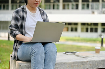 A female college student using her portable laptop on a bench in a campus park.