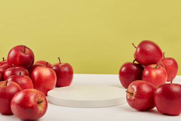 Against a green background, ripe red apples place around a round white empty podium. Space for...