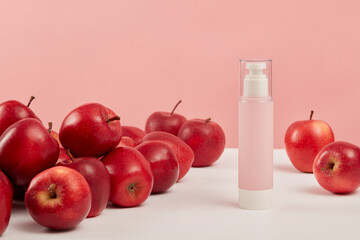 Minimal mockup background for product presentation with pink bottle unlabeled placed on pink background and surround by ripe red apples. Advertising scene for cosmetic of apple extract