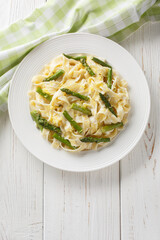 Fettuccine pasta with asparagus, lemon in a creamy cheese sauce close-up in a plate on the table. Vertical top view from above
