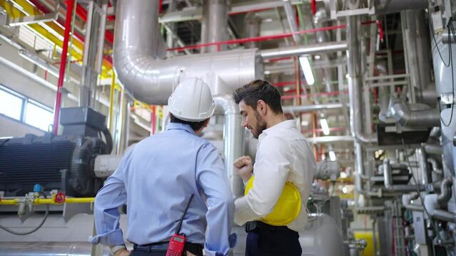 Two professional electrical engineer in safety uniform working together at factory site control room. Industrial engineer worker checking maintenance electric system on laptop computer at plant room.