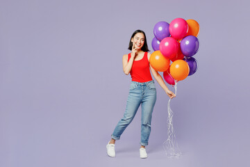 Full body smiling young woman of Asian ethnicity she wear casual clothes red tank shirt hold bunch of colorful air balloons isolated on plain pastel light purple background studio. Lifestyle concept.