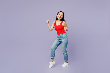 Fototapeta na wymiar Full body smiling happy young woman of Asian ethnicity she wear casual clothes red tank shirt doing winner gesture isolated on plain pastel light purple background studio portrait. Lifestyle concept.
