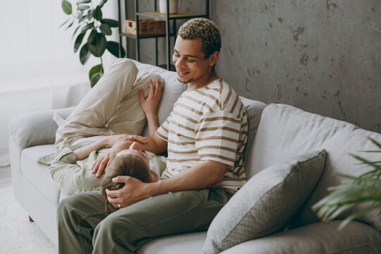 Happy young couple two gay men wearing casual clothes together lying on partner knees sit on sofa couch at home flat rest spend free spare time in living room. Pride day june month love lgbtq concept. - Powered by Adobe