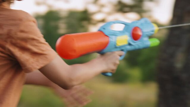 Camera shake of Caucasian elementary age boy shooting water with toy gun in nature at daytime