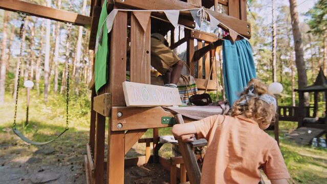 Medium shot of African American and Caucasian elementary age boys drawing no adults sign and climbing into treehouse at daytime