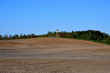A view of a freshly plowed field located next to a tall hill and in a close proximity to a small cottage or village seen on a sunny summer day on a Polish countryside during a hike