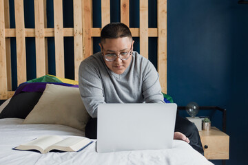 Latin lesbian woman lying on bed using laptop or computer studying at home in Mexico, Hispanic...