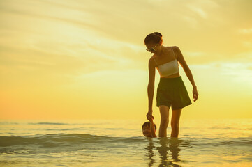 Fototapeta premium Happy family resting at beach in summer, Mother and baby boy feet at the sea foam at the sunlight water is moving