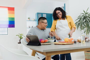 Latin lesbian couple cooking dinner in kitchen at home in Mexico, Hispanic homosexual people from lgbt community with rainbow flag in Latin America