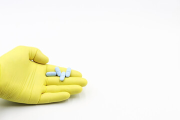 Hand with yellow glove and blue pills. White background. Space for text