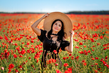 Portrait of a beautiful brunette woman in a poppy field. She's wearing a big hat and a red flower...