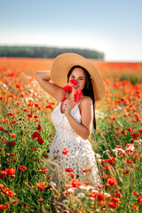 Portrait of a beautiful girl in a field with poppies and daisies . She's wearing a big straw hat...