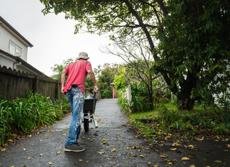 A man pushing a wheelbarrow full of paint cans on the concrete driveway. Home refurbishment do it yourself project.