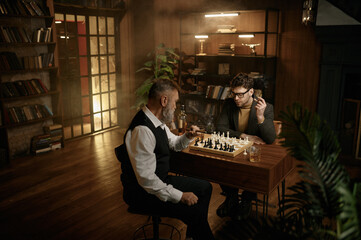 Two man playing chess sitting at table in home living room
