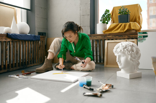 Young female artist drawing picture sitting on floor in her own art studio