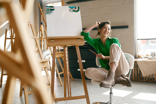 Portrait of overjoyed smiling woman artist holding paintbrush on nose