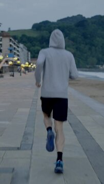 Rear view of sportsman running beside beach. Vertical frame of runner doing exercise.
