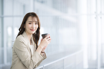 オフィスビルで見上げるスーツ姿の美しい女性　コーヒーを飲んで休憩する　カメラ目線