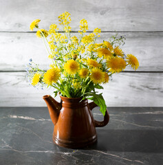 Still life with yellow dandelions in a teapot on a dark marble table. The concept is vivid life.
