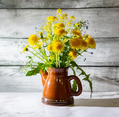 Still life with yellow dandelions in a teapot on a white marble table. The concept is a bright healthy life.