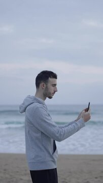 Sportsman taking selfie at the beach. Young man using phone at seaside