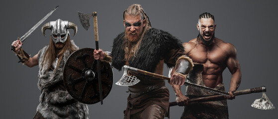 Shot of group of three vikings dressed in fur and armor armed with axes.
