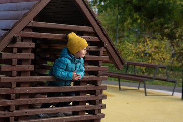 portrait of a happy emotional little boy in a hat and jacket playing on the playground in autumn	