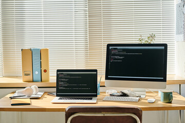 Horizontal image of computers with security codes on the screen standing on workplace of programmer in office