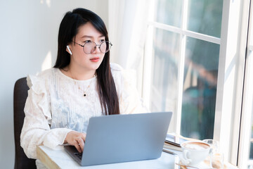 Happy of asian freelance people Businesswoman wearing wireless earphones casual working with laptop computer with a coffee cup mug,Notebook and smartphone at the cafe,Business Lifestyle communication