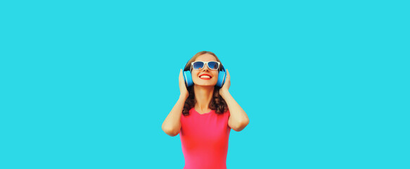 Portrait of happy smiling young woman in wireless headphones listening to music on blue background
