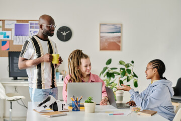 Obraz premium Group of young programmers discussing project in team sitting at table with laptop in office