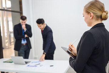 Side view of young secretary or businesswoman Use a tablet to take meeting notes. Confident working female secretary clerk standing in office at team meeting