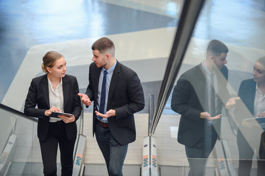 A business man and two business women using a digital tablet talking while walking on the escalator business people work together to work at the office