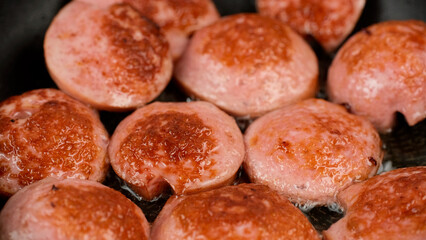 Cooking sausages in pan, close up. Fry sliced sausages