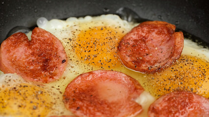 Cooking fried eggs and sausages in pan, close up