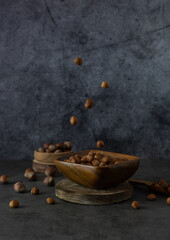 Peeled hazelnuts hang in the air above a wooden bowl. Nuts on a dark table. Dark gray background