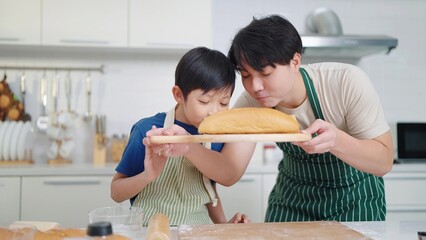 Father and son baker wearing apron sniffing aroma from bread after baked. Enjoy smelling fresh bread. Food and cuisine concept, Happy asian family