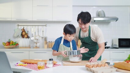 Asian single father teaching son cooking or baking spending time on holidays together in kitchen...