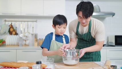 Asian single father teaching son cooking or baking spending time on holidays together in kitchen...